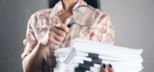 Mujer con documentos en la mano utilizando lupa para implementar herramientas de gestión documental con Legarchivo